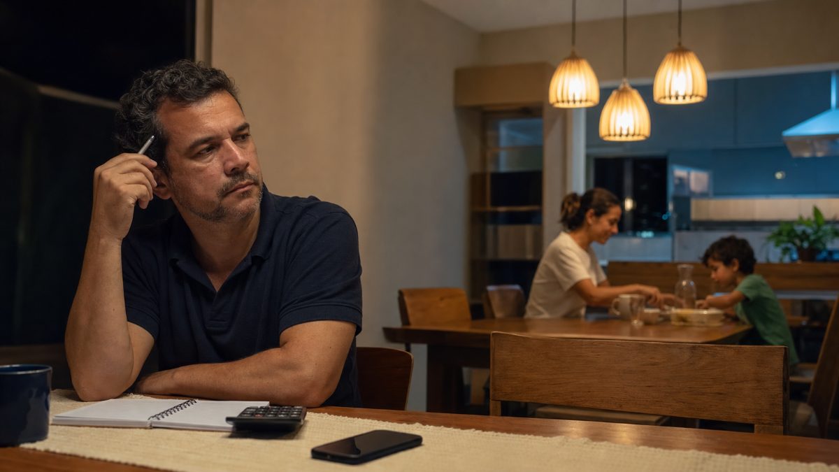 Empresário pensativo à noite enquanto a família janta ao fundo